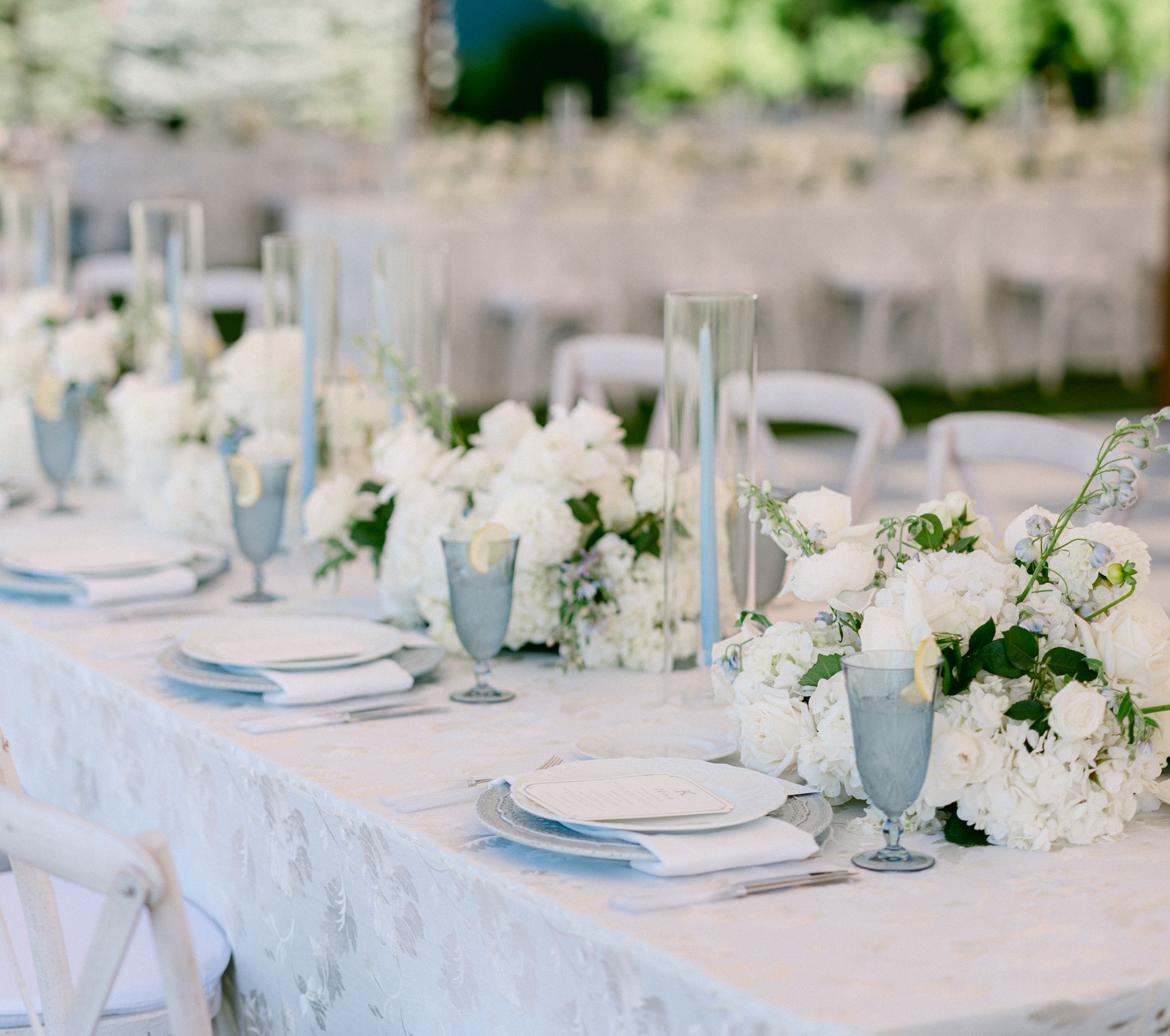 An elegant table setting featuring white china, white flower bouquets, and several wine glasses and flutes