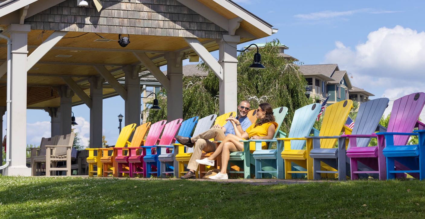 A couple relaxes in multi-colored Adirondack chairs taking in the river view