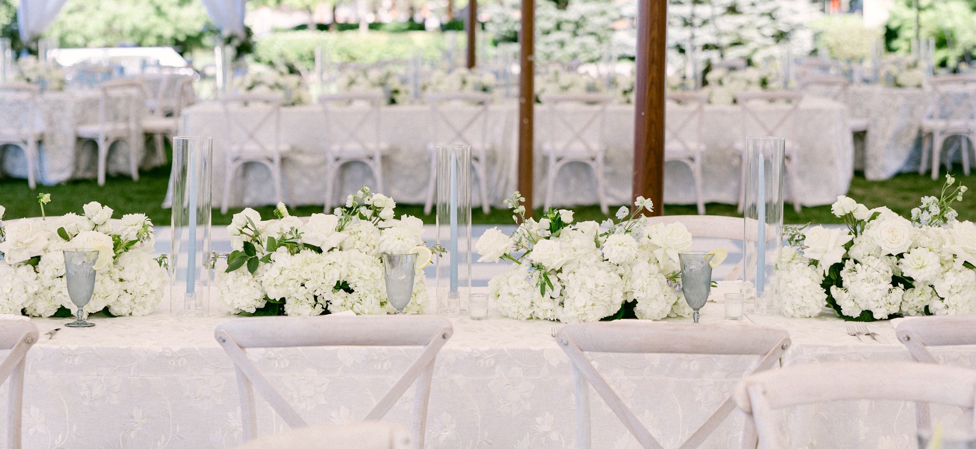 A row of white bouquets on a table under an outdoor tent set for a wedding