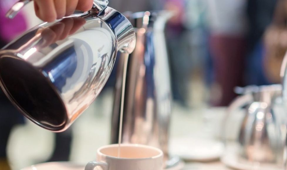 A server pouring cream into a coffee at a table in a conference room