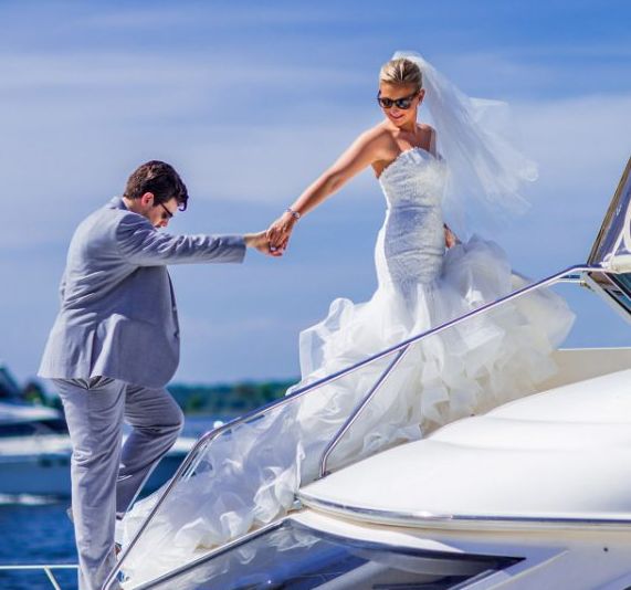 A couple in wedding attire carefully boarding a boat