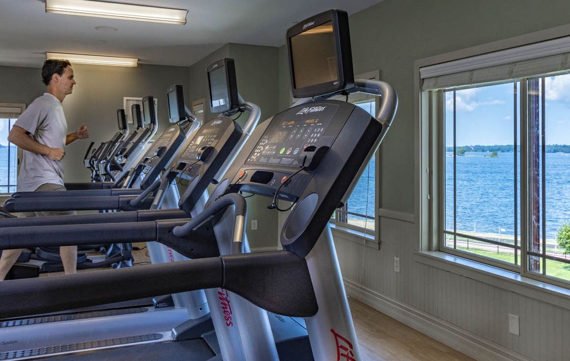 A runner is on a treadmill in the fitness center with a view of the river out the window