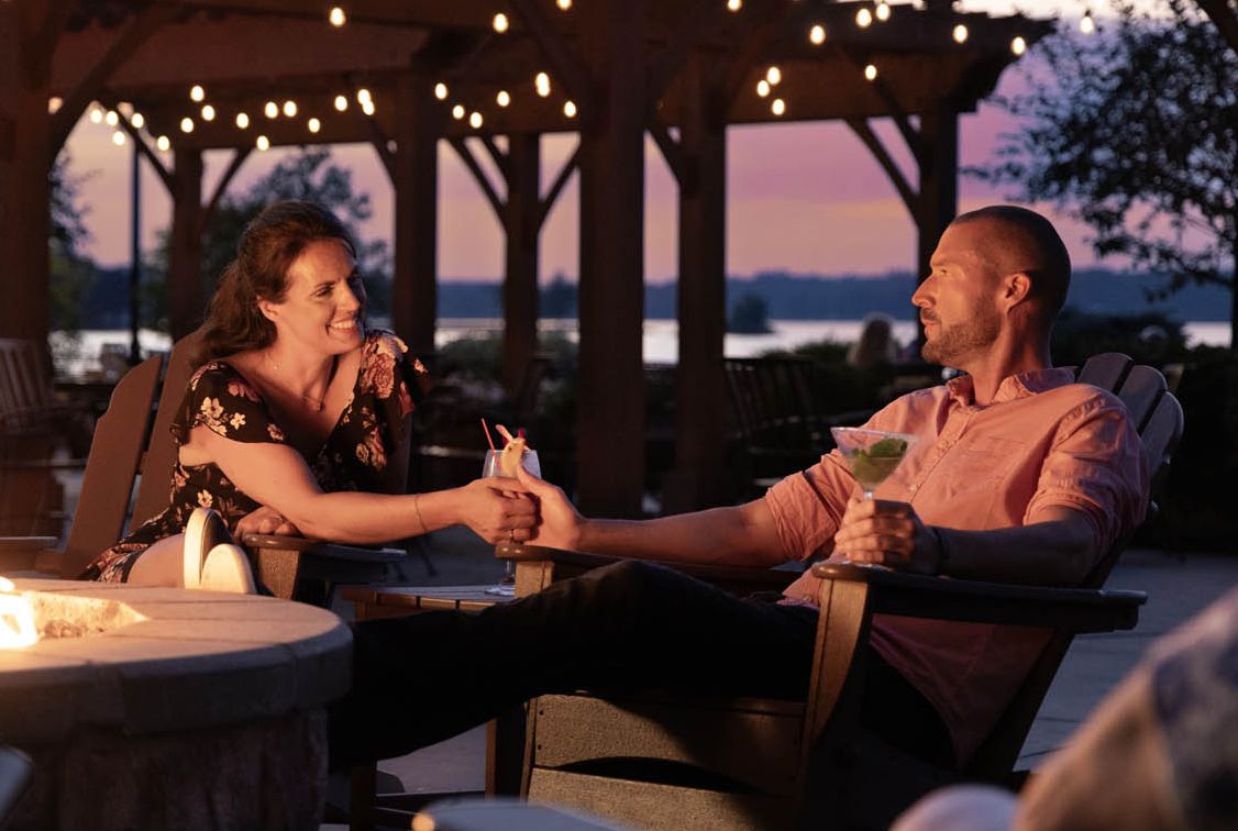 A couple relaxes by the fire pits with custom crafted cocktails at the 1000 Islands Harbor Hotel